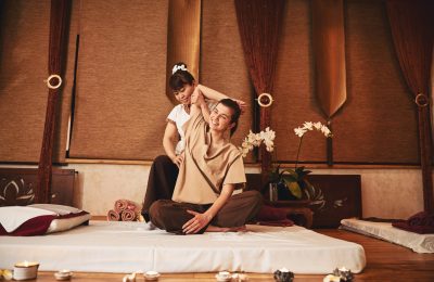 Asian massage specialist lifting right arm of smiling woman while pressing her palm to client waist